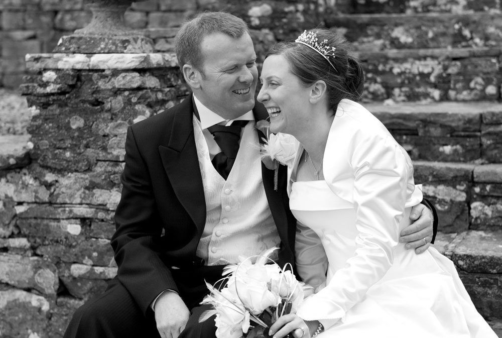 Simonstone Hall Hotel wedding of Alison and Hamish - The couple sat on the steps outside the venue - laughing naturally in monochrome - Authentic wedding photography across Yorkshire by Tim Christian Jones | Leeds wedding photographer.